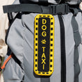 Load image into Gallery viewer, Southlake Paws Dog Taxi Patch featuring a black background with yellow text and paw print, attached to a gray backpack.