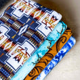 Load image into Gallery viewer, Oversized fleece throw blanket by Southlake Paws, featuring various colorful patterns stacked neatly. Size: 60" x 84".