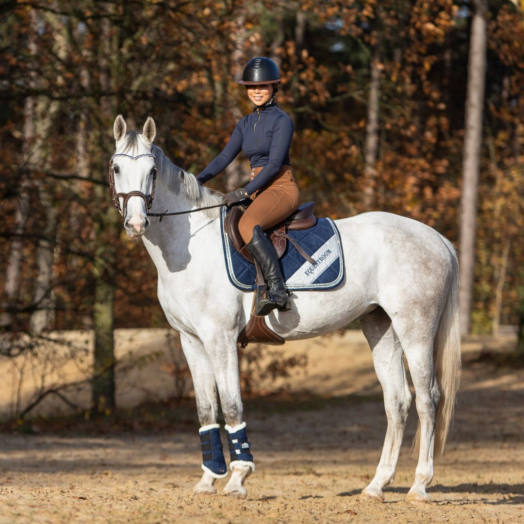 Southlake Paws Blue Astra Saddle Pad Set on a gray horse, rider in navy top and brown pants, autumn forest background.