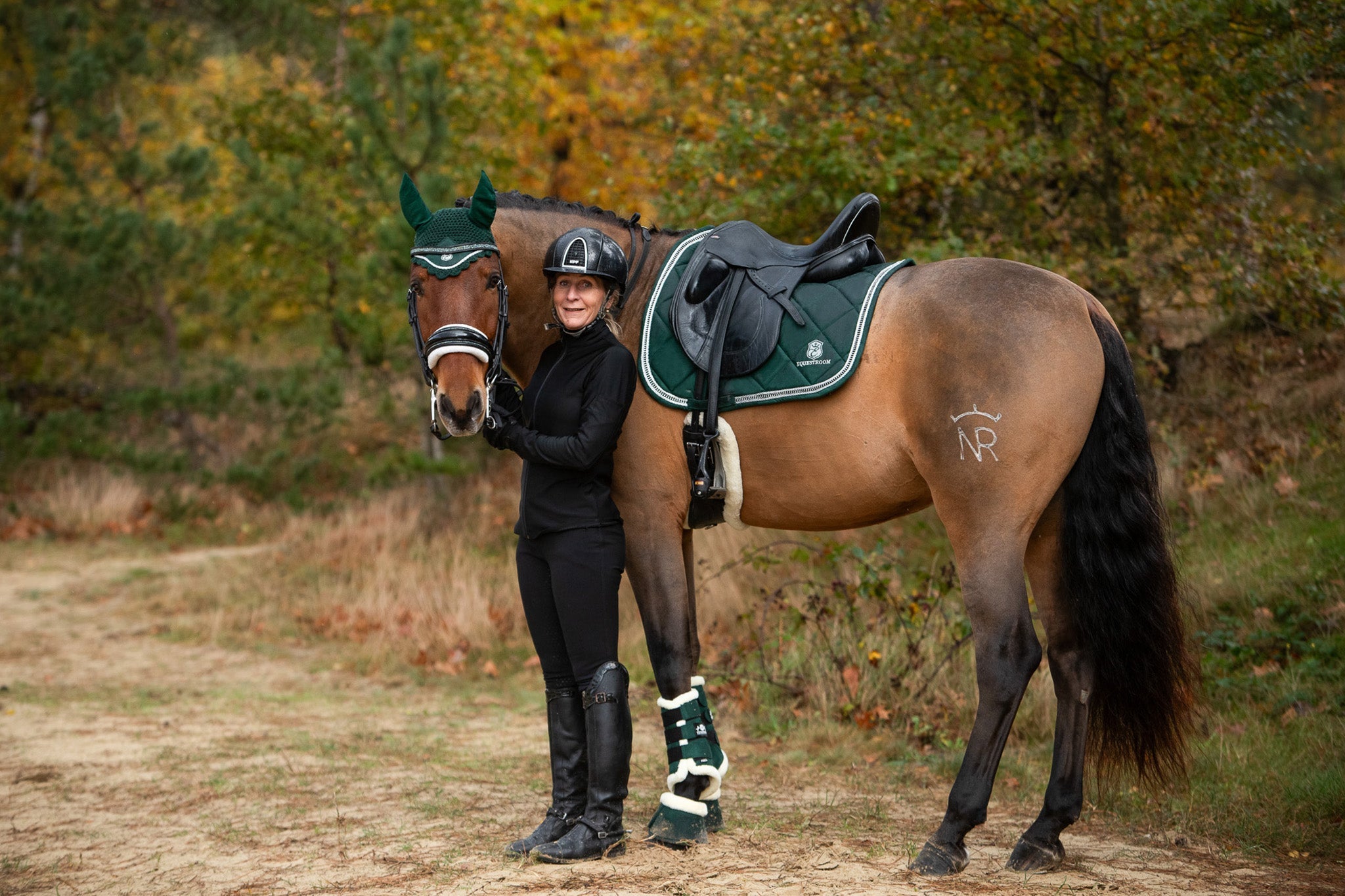 Southlake Paws Pine Grove Saddle Pad on a horse, with a rider in black attire, surrounded by autumn foliage.