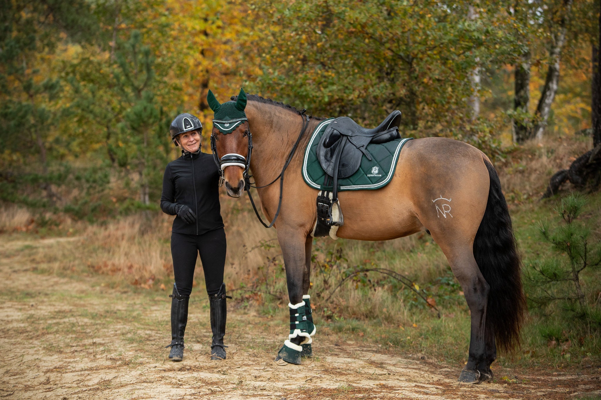 Southlake Paws Pine Grove Saddle Pad displayed on a horse, with a rider in black attire standing beside it in a forest settin