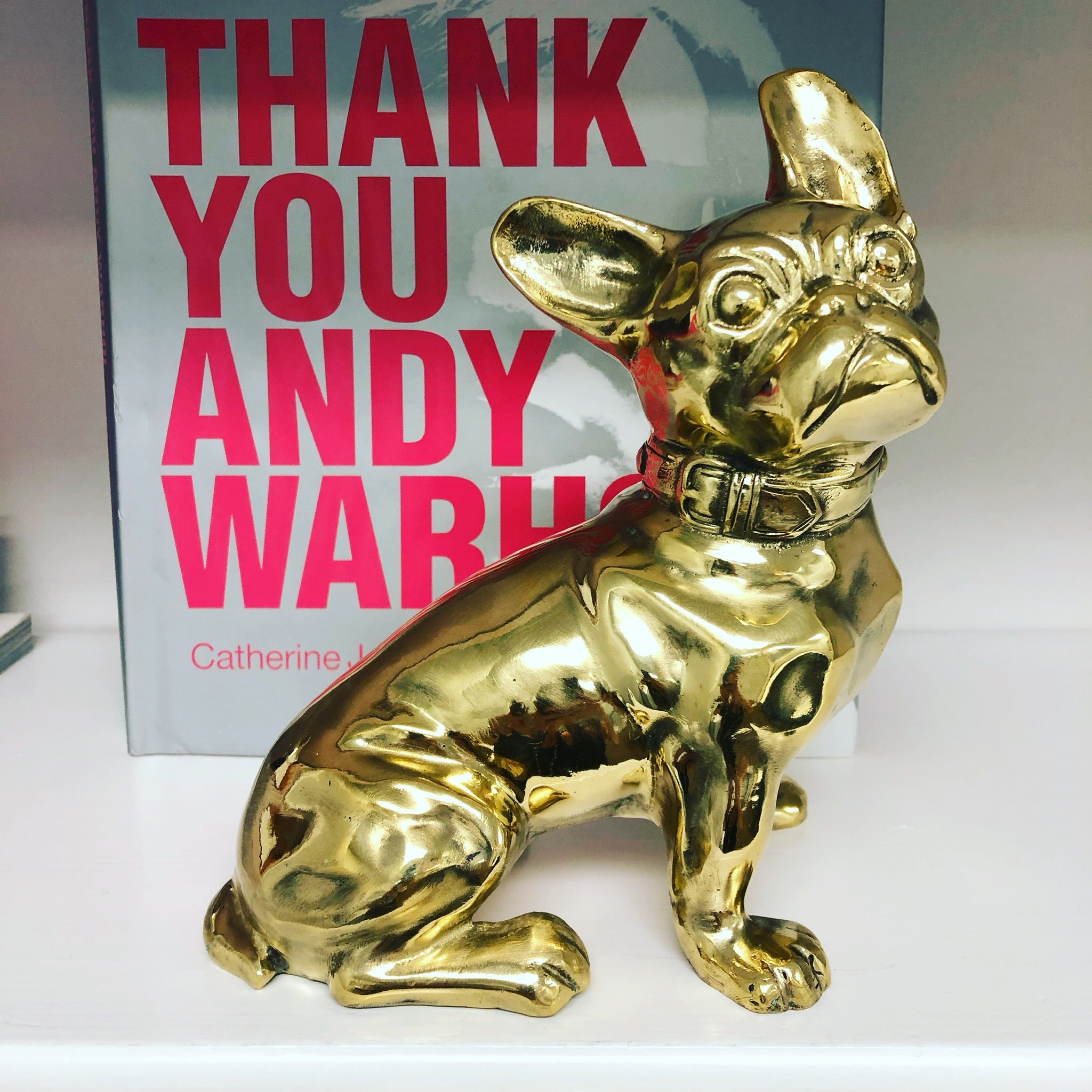 Gold dog figurine in front of a book titled 'Thank You Andy Warhol' by Catherine