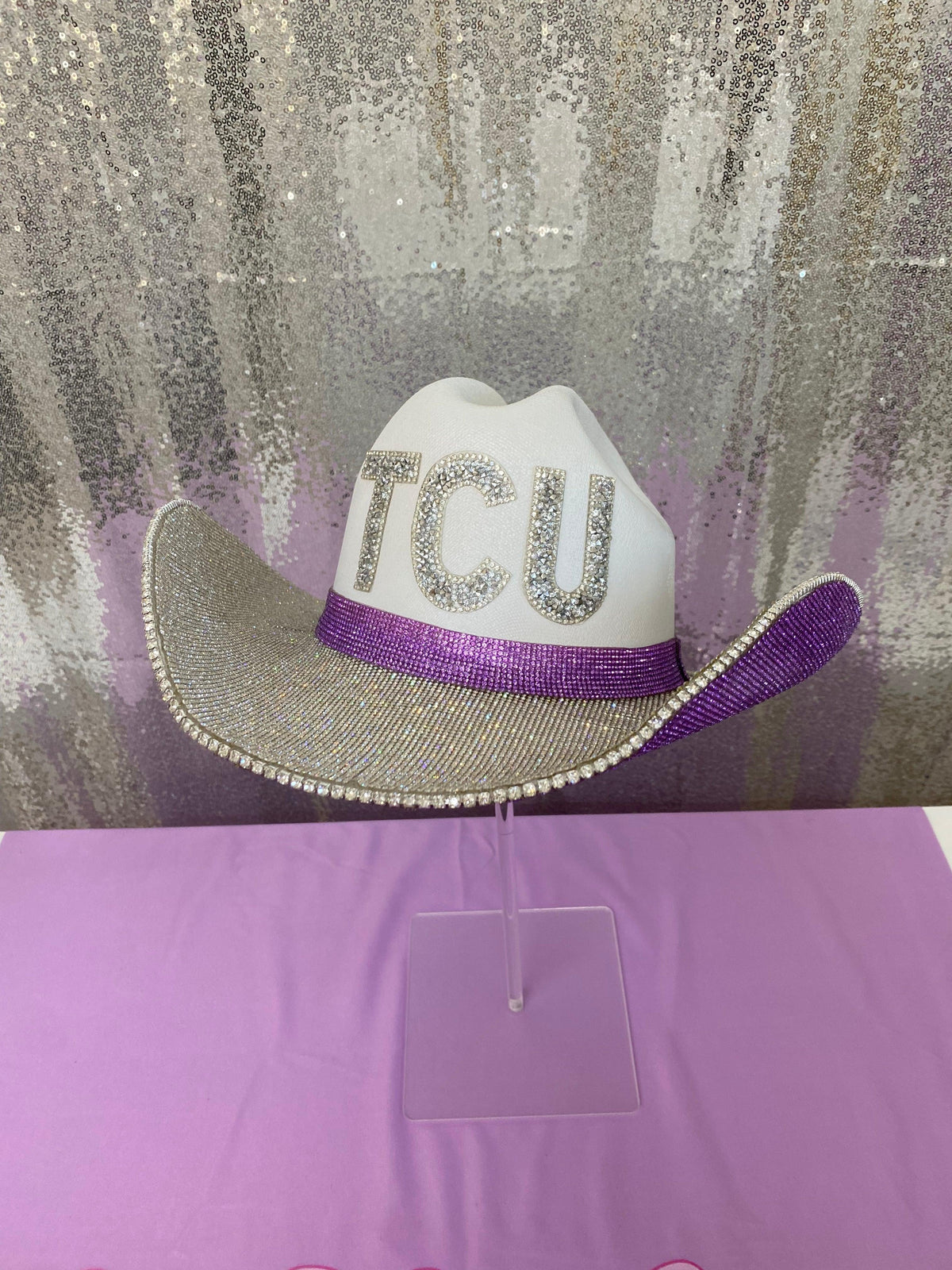 White cowboy hat with 'TCU' on a glittery background
