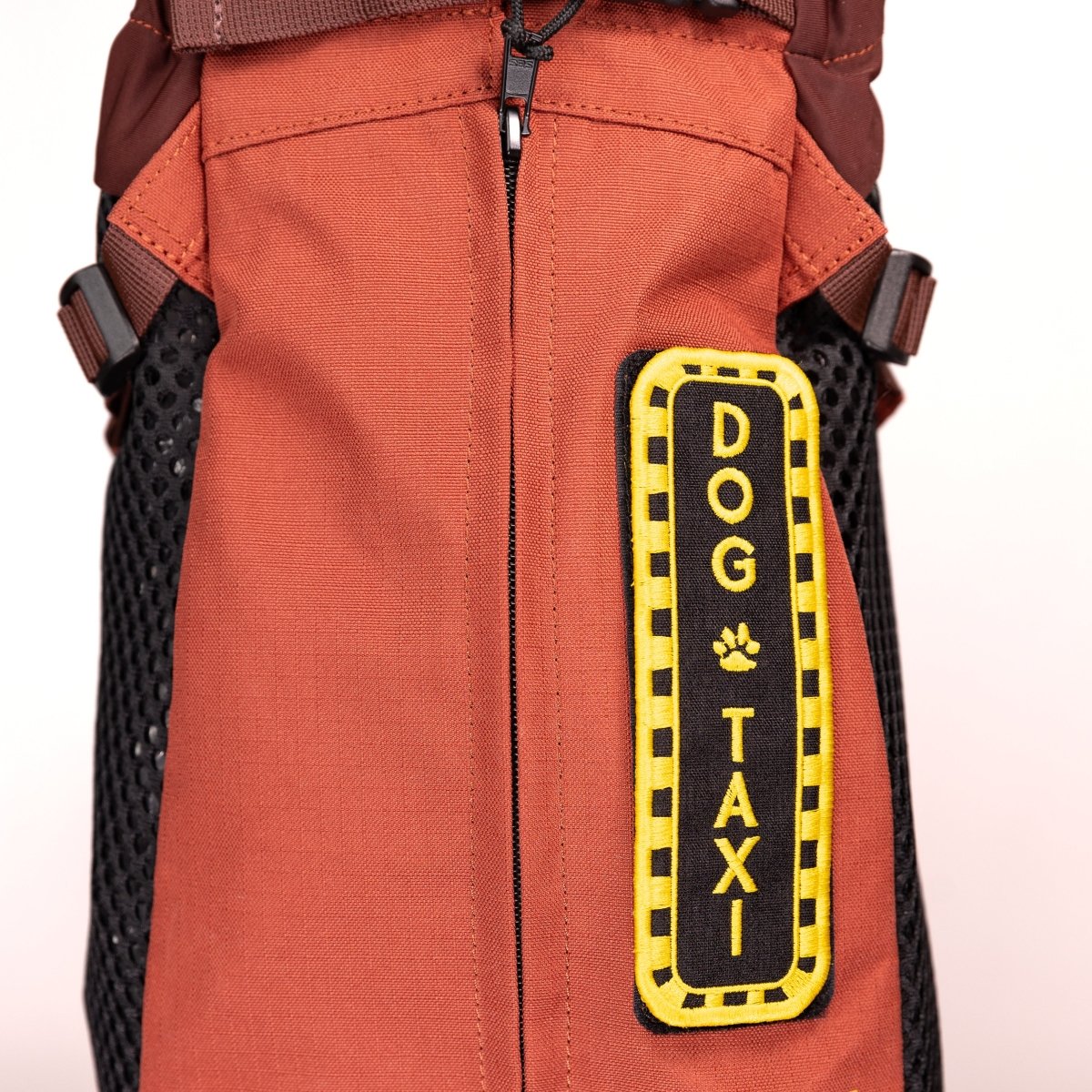 Orange dog backpack featuring a black and yellow "DOG TAXI" patch with a paw print design. Ideal for pet transport.