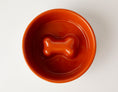 Load image into Gallery viewer, Orange slow feeder dog bowl with anti-slip stainless steel base, featuring a bone-shaped design in the center.
