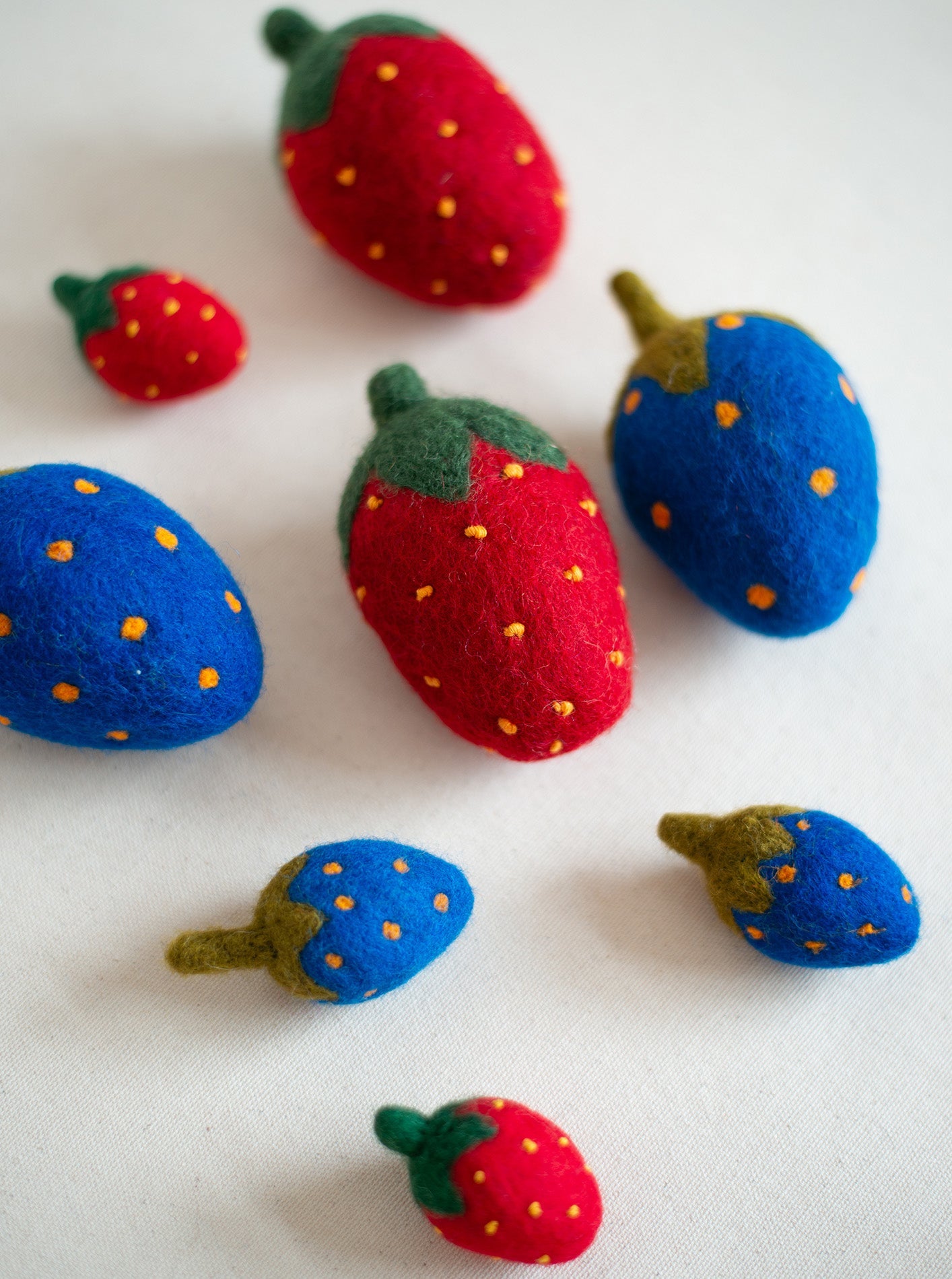 Colorful felt dog toys shaped like strawberries in various sizes, featuring red and blue colors with green leaves and yellow 