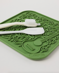 Load image into Gallery viewer, Green silicone lick mat with raised designs, featuring a guitar and the word "Howdy," accompanied by a white spatula and toot
