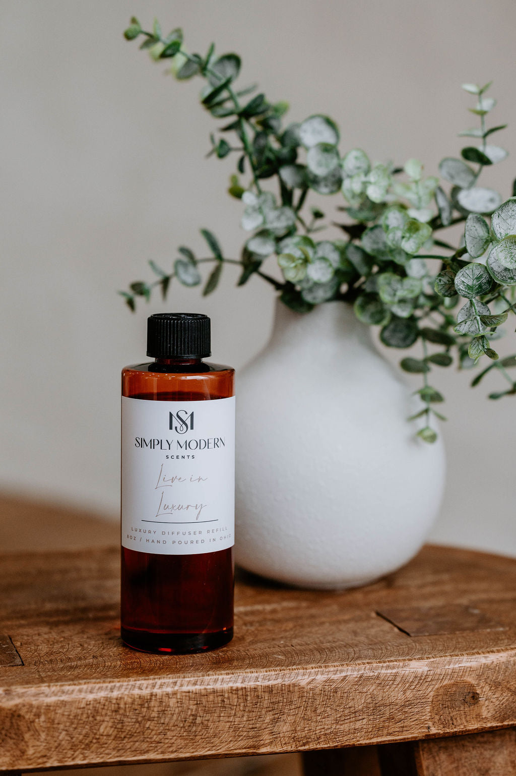 Luxury Electric Diffuser 8 OZ Refill by Southlake Paws, displayed next to a vase with greenery on a wooden table.