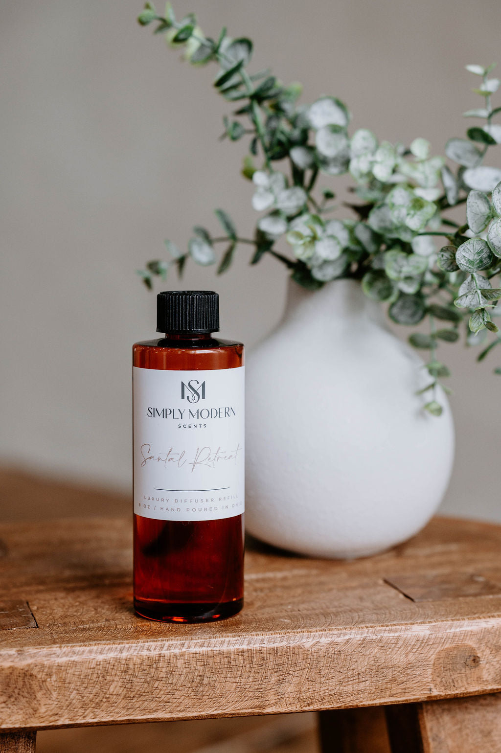 Luxury Electric Diffuser refill by Southlake Paws, 8 oz bottle on a wooden table with a decorative vase and greenery.