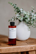 Load image into Gallery viewer, Luxury Electric Diffuser 8 OZ Refill by Southlake Paws, featuring a bottle with a black cap on a wooden table beside a vase w
