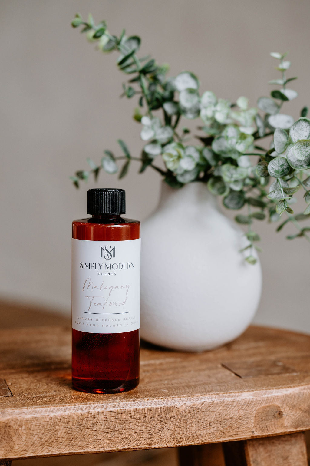 Luxury Electric Diffuser 8 OZ Refill by Southlake Paws, featuring a bottle with a black cap on a wooden table beside a vase w