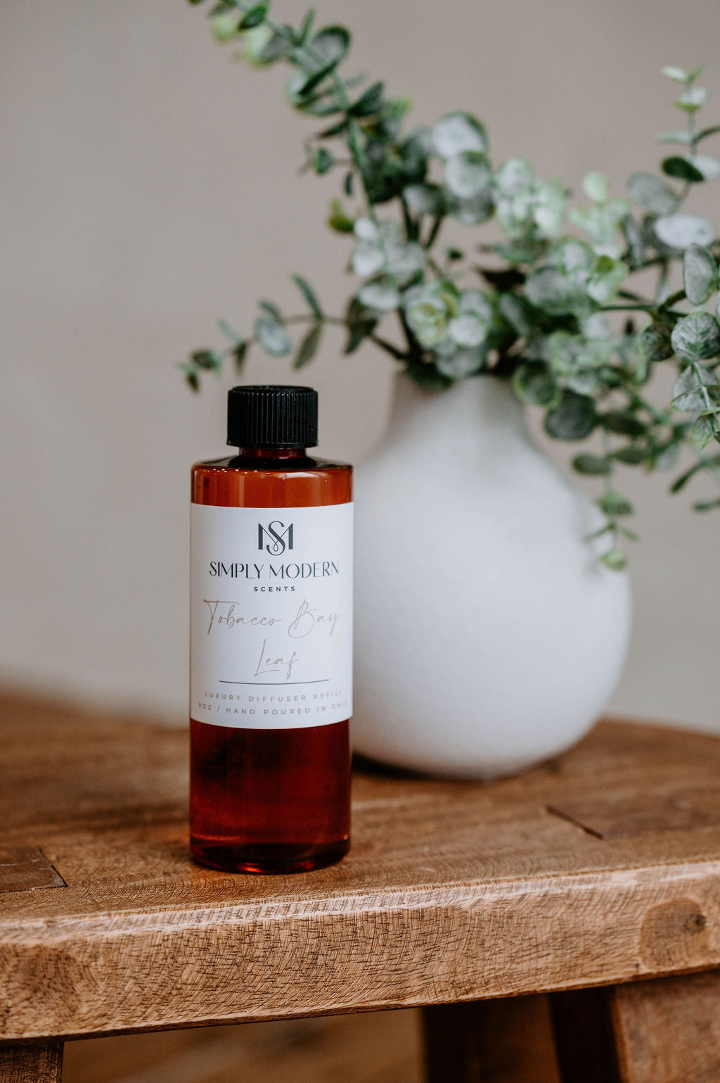 Luxury Electric Diffuser 8 OZ Refill by Southlake Paws, featuring a sleek bottle on a wooden table with greenery in the backg