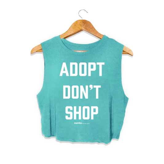 Turquoise crop top with bold white text reading "ADOPT DON'T SHOP," designed for dog lovers. Made in the USA.