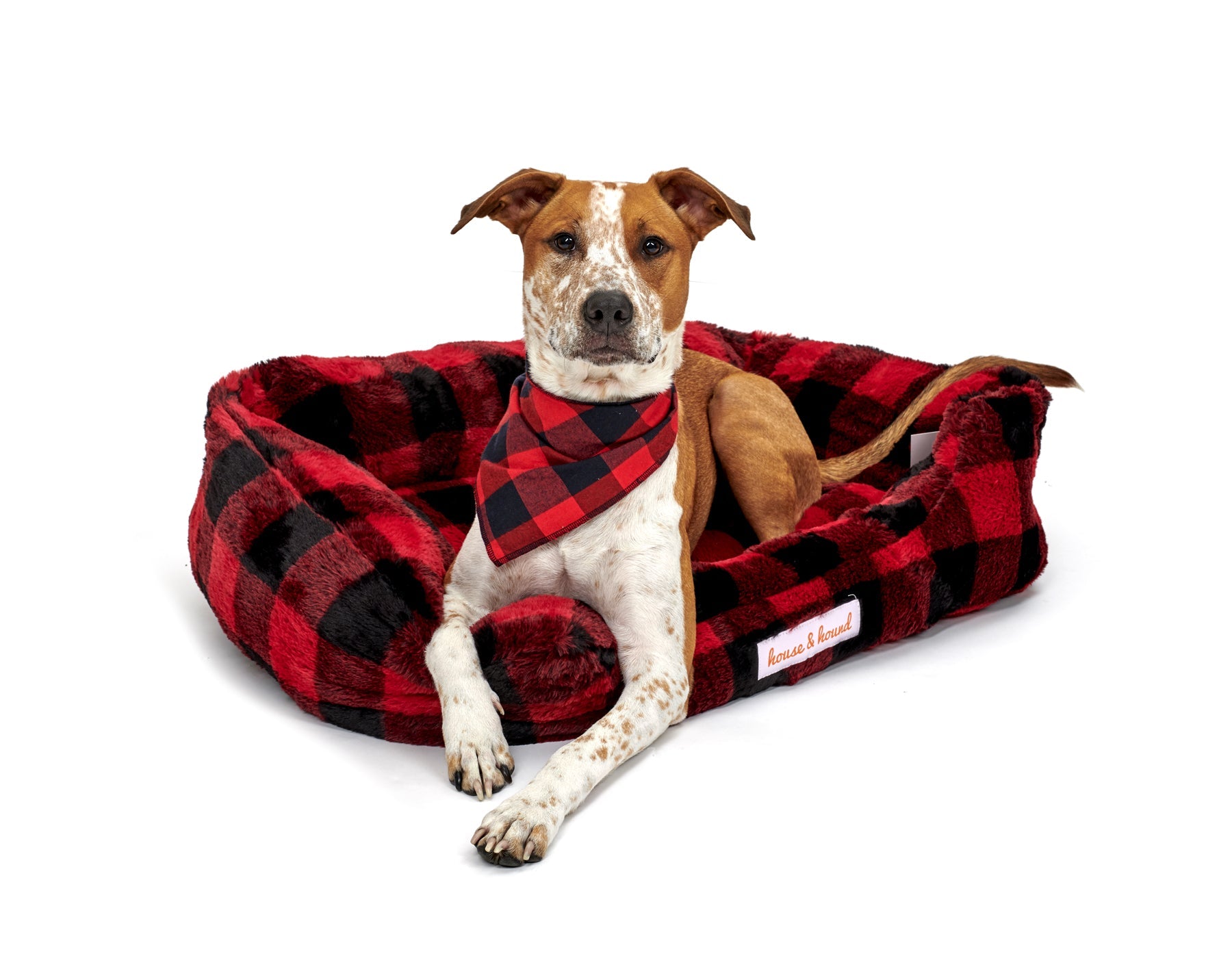 Red and black plaid Mink Relaxer Bed by Southlake Paws with a dog wearing a matching bandana lounging on it.