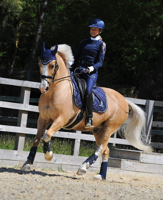 Deep Sapphire Saddle Pad Set by Southlake Paws featuring a rider in navy attire on a palomino horse in a riding arena.