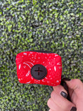 Load image into Gallery viewer, Red Paisley Poop Bag Holder by The Modern Dog Company, featuring a zippered design and a button closure, held against a green
