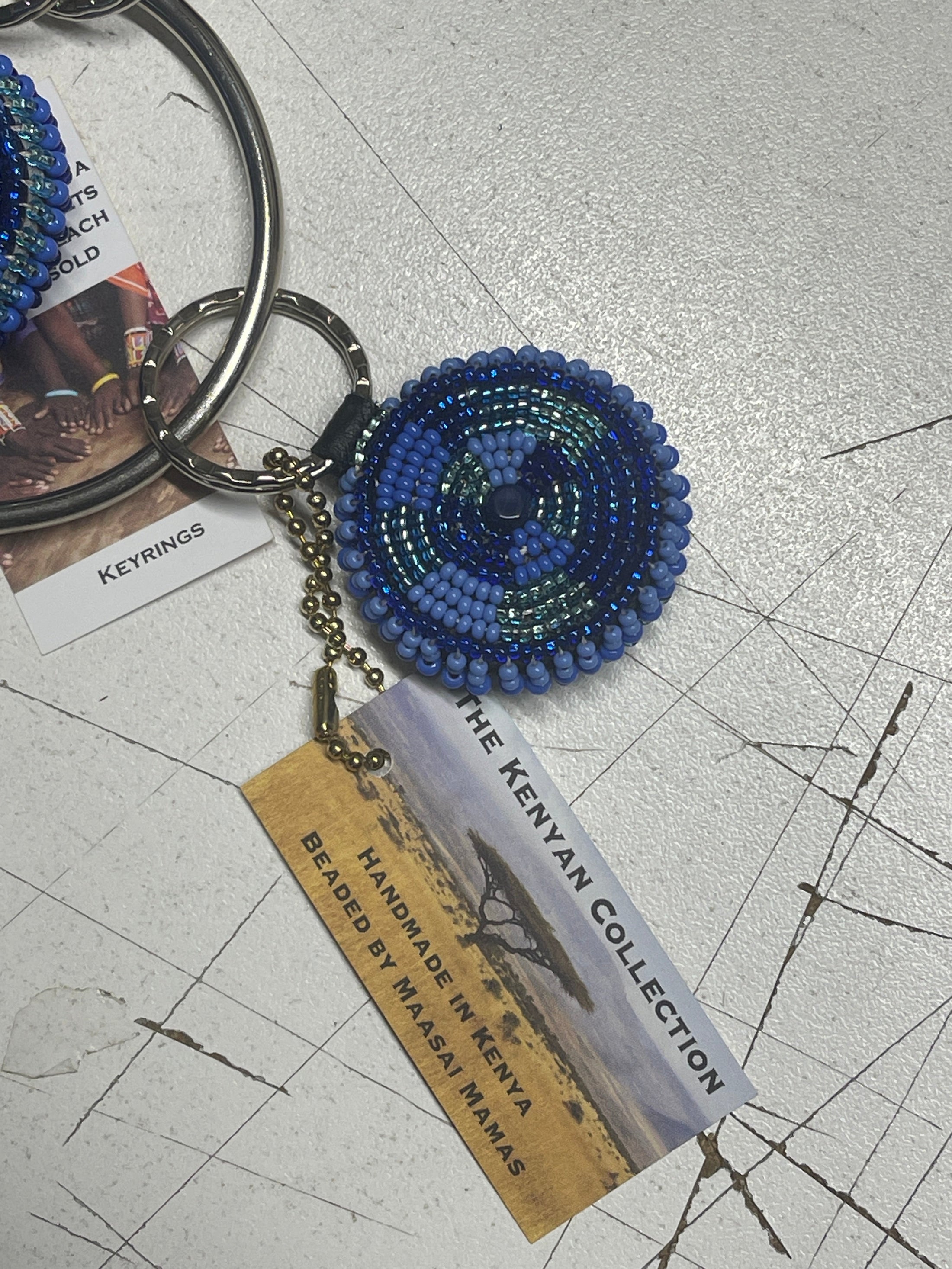 Beaded keychain from Southlake Paws featuring a circular blue design, attached to a keyring with a tag about its Kenyan origi