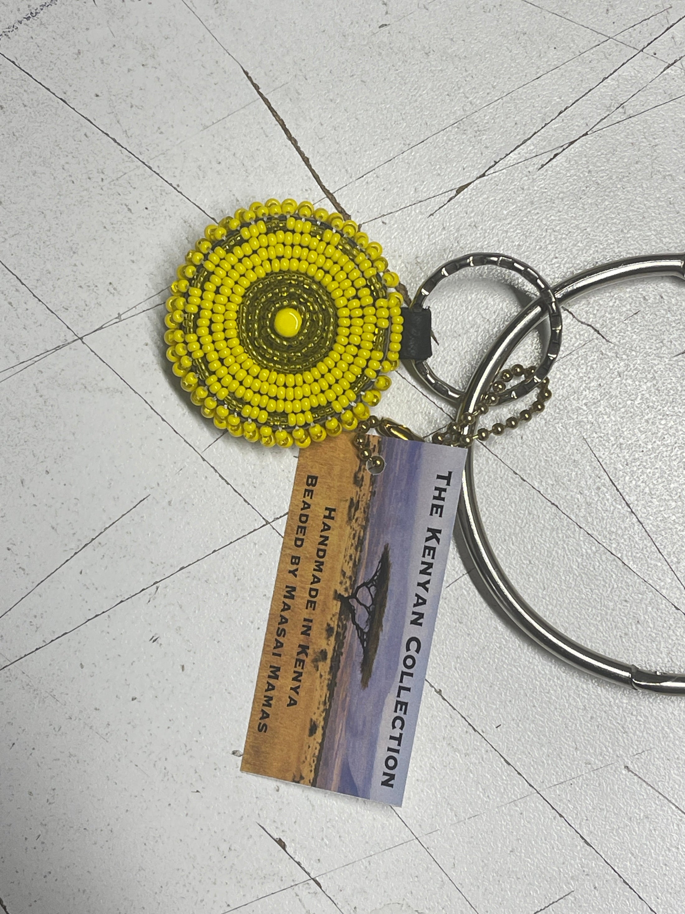Yellow beaded keychain with a circular design, attached to a metal keyring, featuring a tag that reads "The Kenyan Collection