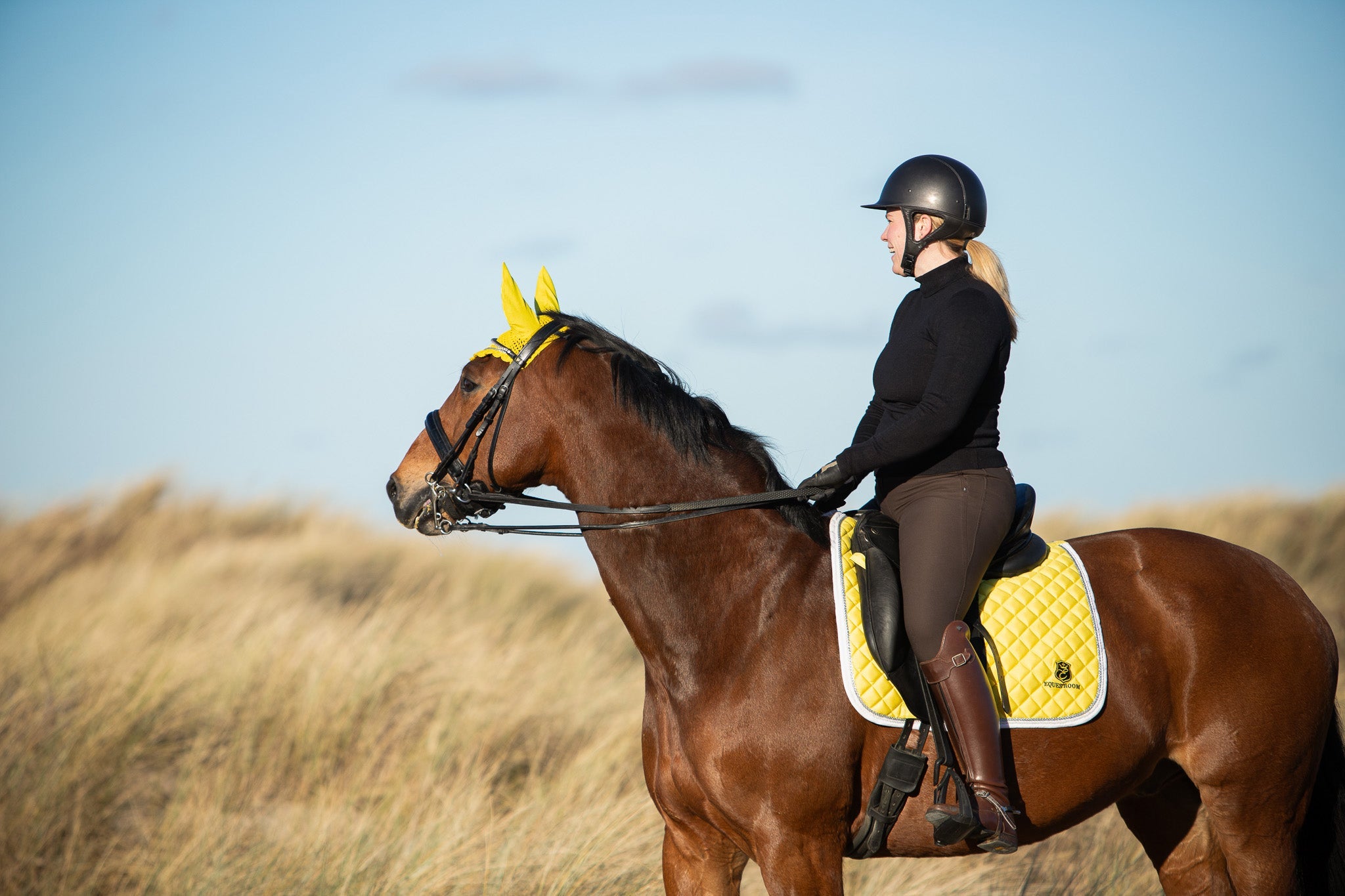 Southlake Paws Mimosa Saddle Pad in yellow on a brown horse, rider wearing a black helmet and outfit, standing in a grassy fi