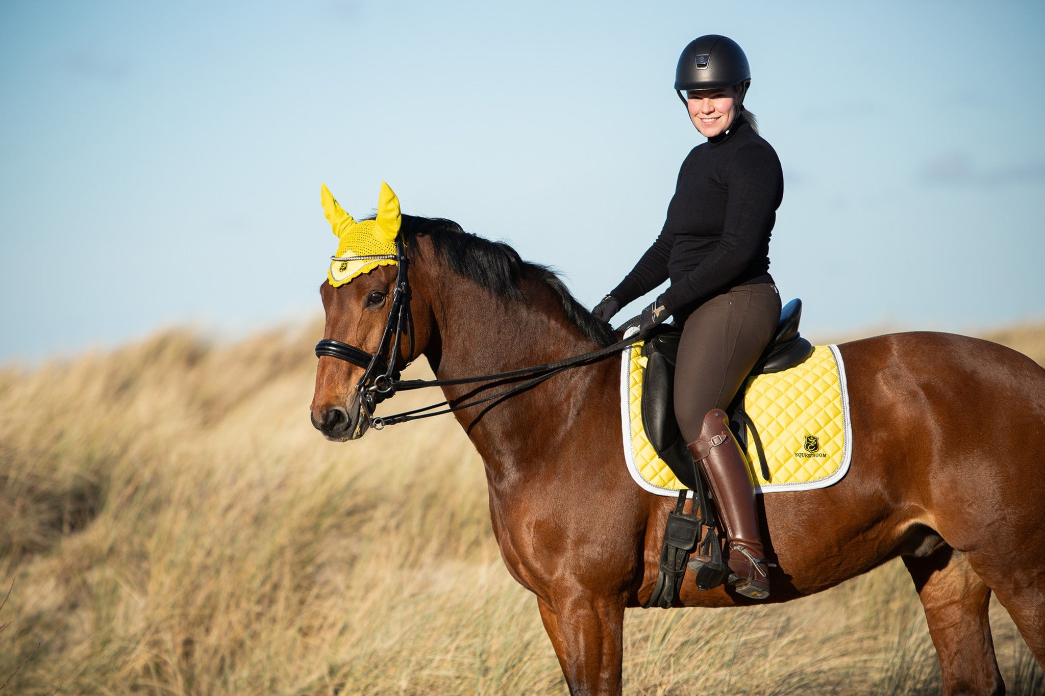 Southlake Paws Mimosa Saddle Pad on a brown horse, rider in black attire and helmet, yellow ear bonnet, sunny outdoor setting