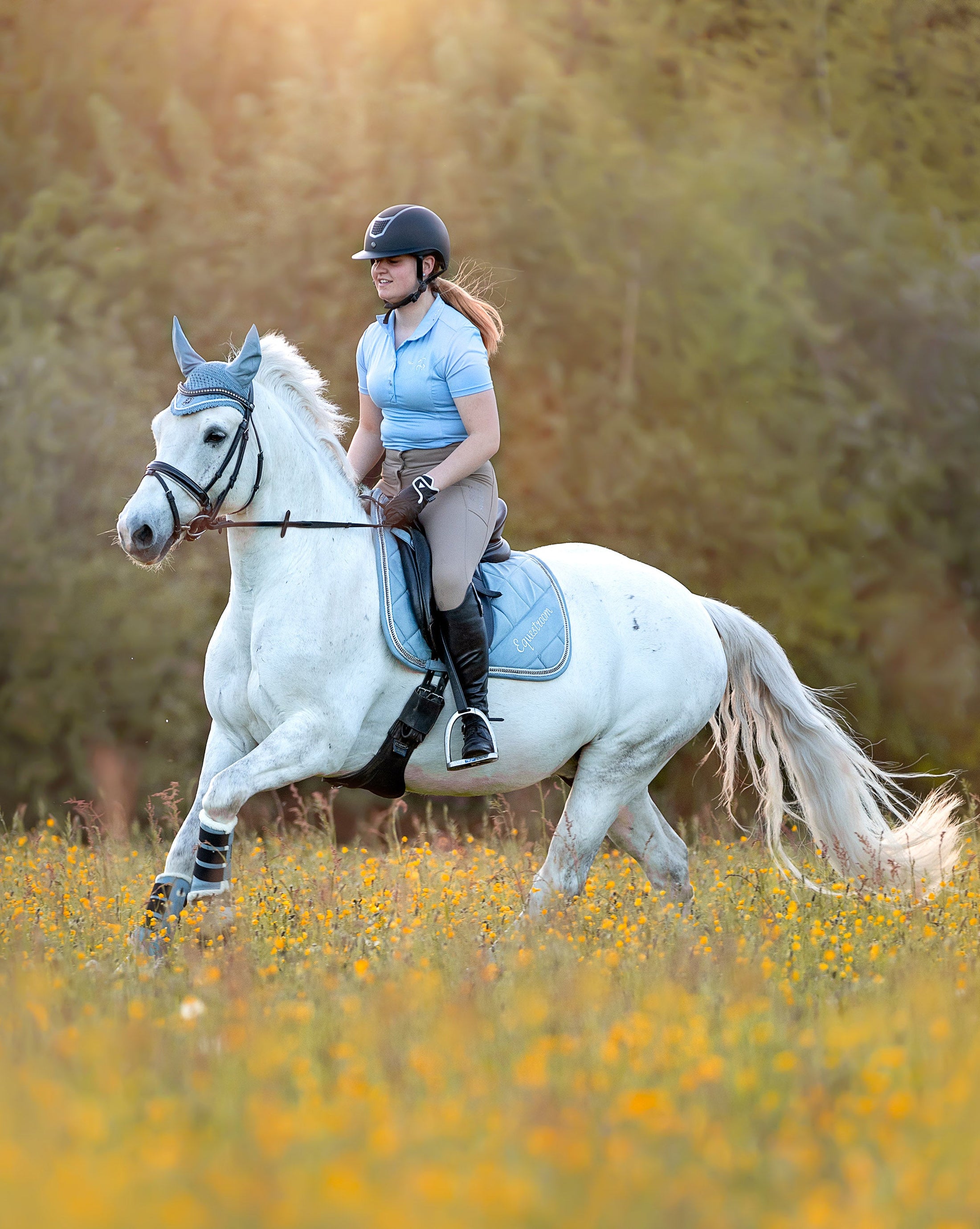 Southlake Paws Moonstone Blue Saddle Pad on a white horse, rider in a blue shirt, galloping through a field of flowers.
