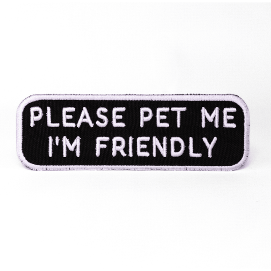 Black rectangular patch with white text reading "PLEASE PET ME I'M FRIENDLY" from Southlake Paws.